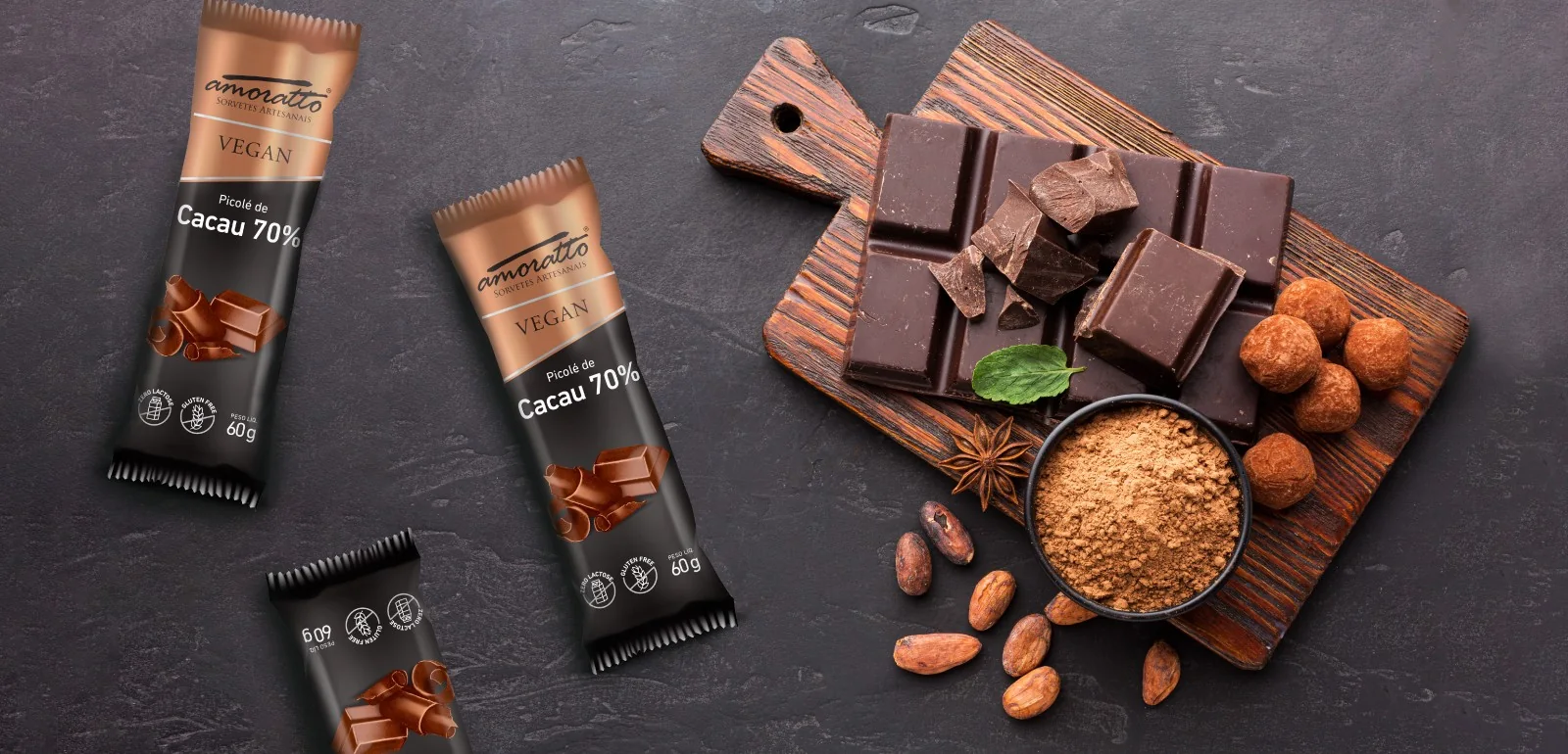 Picolés Amoratto de cacau 70% sobre ardósia, ao lado de chocolate, cacau em pó e amêndoas de cacau.